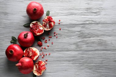 Gri ahşap arka planda tohum ve yapraklarla taze olgun narlar.