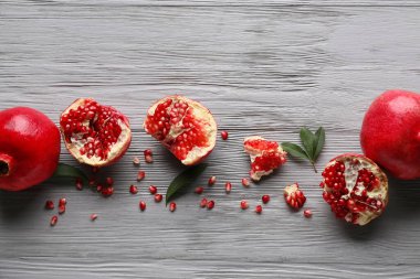 Gri ahşap arka planda tohum ve yapraklarla taze olgun narlar.