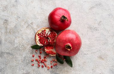 Gri arka planda tohum ve yapraklarla taze olgun narlar.