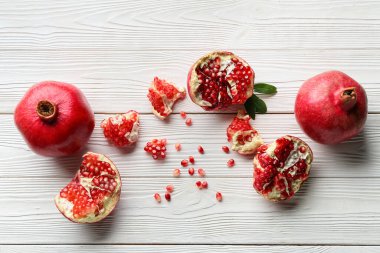 Tohumlarla taze nar ve beyaz ahşap arka planda yapraklar.