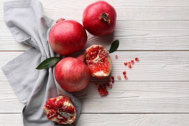 Tohumlarla taze nar ve beyaz ahşap arka planda yapraklar.