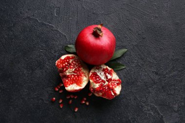 Koyu arkaplanda tohum ve yapraklarla taze olgun nar.