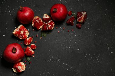 Siyah zemin üzerinde tohum ve yapraklarla taze olgun narlar.