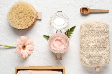 Doğal vücut fırçası kavanozu, banyo malzemeleri ve hafif arka planda çiçek içeren kompozisyon