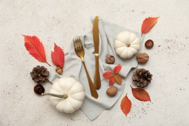 Sonbahar yapraklı şık çatal bıçak takımı, farklı fındıklar, kozalaklar ve beyaz arka planda taze balkabakları.
