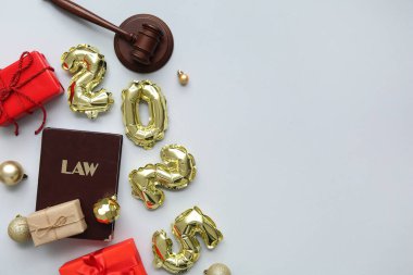 Hakim tokmağı, hukuk kitabı, hediyeler ve gri arka planda Noel toplarıyla 2025 'i düşün.