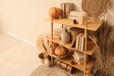 Balkabaklı raf ünitesi, sonbahar süslemeleri ve bej duvarlı kitaplar.