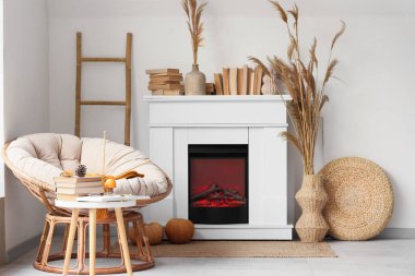 Koltuğu, şöminesi, sonbahar süslemeleri ve sehpası üzerinde kitapları olan aydınlık oturma odasının içinde.