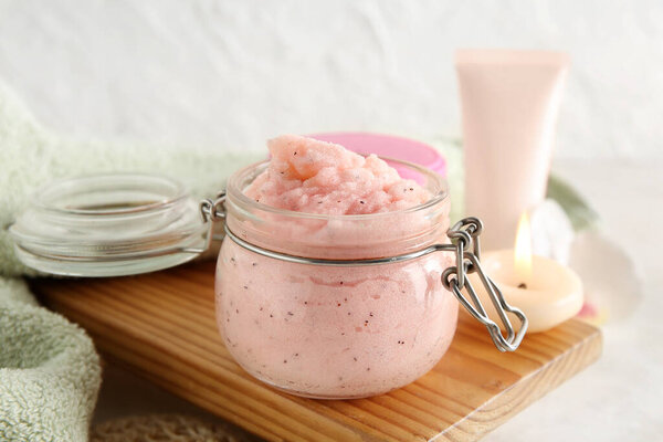 Jar of natural body scrub, burning candle and cosmetics on light background