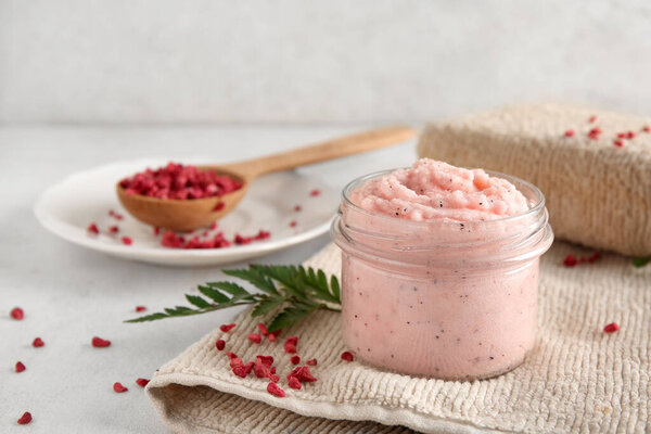 Jar of natural body scrub, freeze-dried raspberries and bath sponge on light table