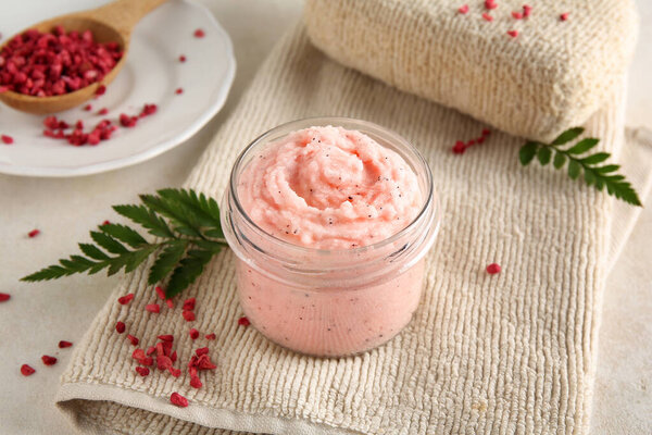 Jar of natural body scrub, freeze-dried raspberries and bath sponge on light table