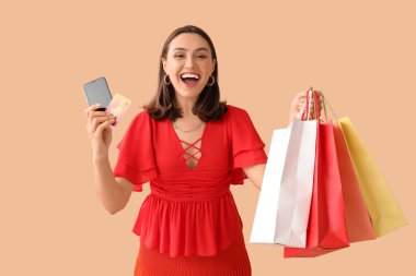 Kredi kartı, cep telefonu ve bej arka planda alışveriş torbaları olan genç bir kadın.