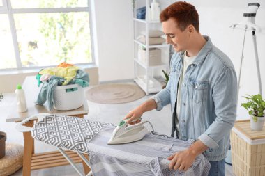 Çamaşır odasında giysileri ütüleyen yakışıklı genç adam.