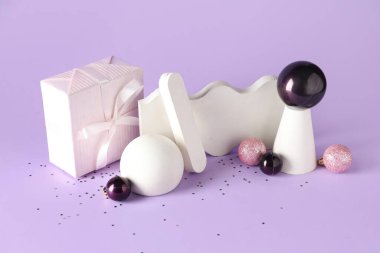 Decorative stands with different Christmas balls and gift box on lilac background clipart