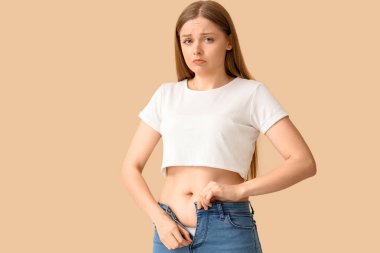 Bej arka planda dar kotlar iliklemeye çalışan üzgün genç bir kadın. Kilo alma kavramı