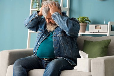 Oturma odasındaki kanepede oturan üzgün yaşlı adamın portresi.