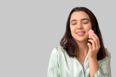 Gri arka planda makyaj süngeri olan güzel bir genç kadın.