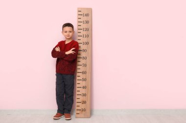 Pembe duvarın yanında boyunu ölçen sevimli küçük bir çocuk.