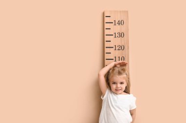 Bej arkaplanla boy ölçüşen sevimli küçük kız.