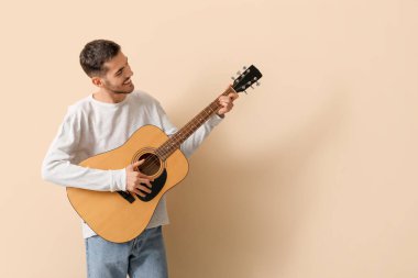 Bej arka planda gitar çalan yakışıklı genç adam.