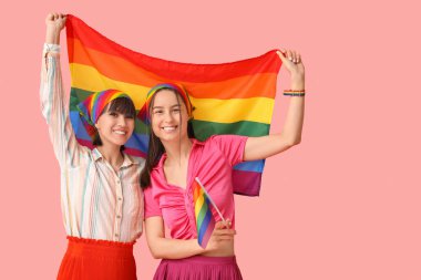 Pembe arka planda LGBT bayrakları olan genç lezbiyen çift