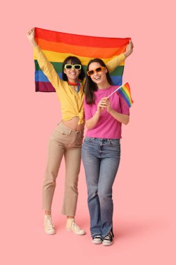 Pembe arka planda LGBT bayrakları olan güneş gözlüklü genç lezbiyen çift