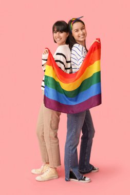 Pembe arka planda LGBT bayrağı olan mutlu genç lezbiyen çift