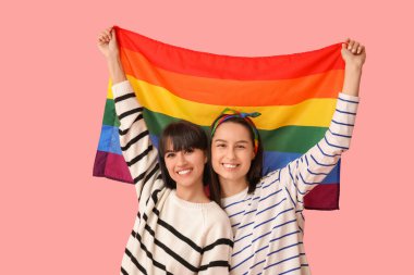 Pembe arka planda LGBT bayrağı olan mutlu genç lezbiyen çift