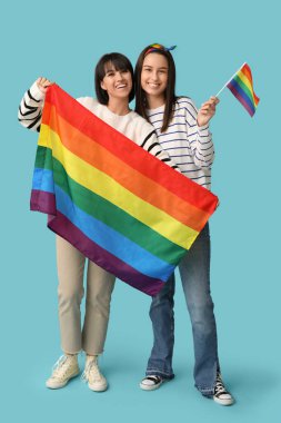 Mavi arka planda LGBT bayrakları olan mutlu genç lezbiyen çift