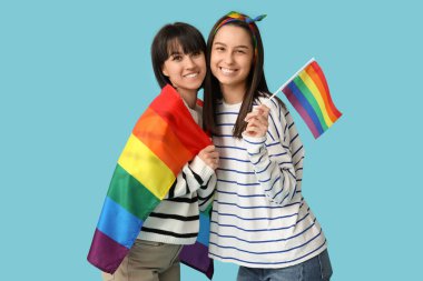 Mavi arka planda LGBT bayrakları olan mutlu genç lezbiyen çift