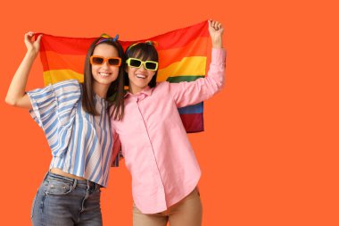 Turuncu arka planda LGBT bayrağı olan genç lezbiyen çift