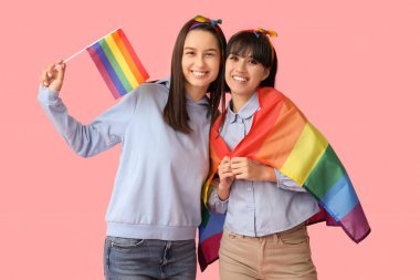 Pembe arka planda LGBT bayrakları olan genç lezbiyen çift