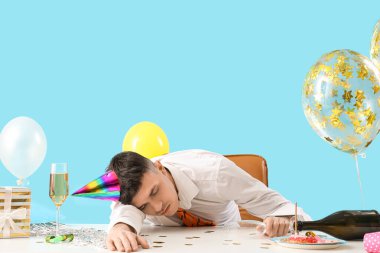 Akşamdan kalma genç iş adamı mavi arka planda doğum günü partisinden sonra masada uyuyor.