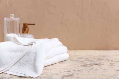 Temiz yumuşak havlular, bir şişe kozmetik ürünü ve kahverengi duvarın yanında pamuk yastıklı tutucu.