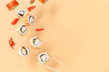 Bej arka planda lezzetli uçan suşi ruloları, zencefil ve çubuklar.