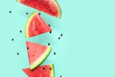 Uçan taze karpuz parçaları ve turkuaz arka planda tohumlar.
