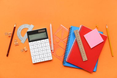 Turuncu arka planda hesap makinesi ve okul kırtasiyesi