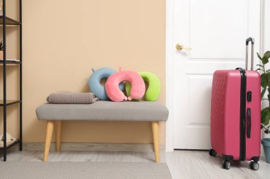 Koridordaki kapının yanındaki bankta pembe valiz ve yastıklar. Seyahat kavramı