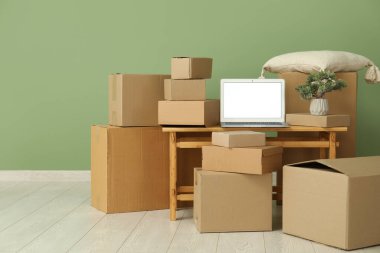 Boş dizüstü bilgisayar, taşınan kutular ve yeşil duvarın yanındaki bonsai ağacı.