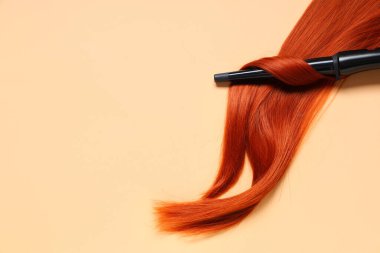 Bej arkaplanda kızıl saçlı saç maşası.