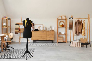 Moda tasarımcısının stüdyosunun içinde manken, elbise rafı ve çekmeceler var.