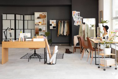 Moda tasarımcısının stüdyosunun içinde masalar, mankenler ve elbise rafları var.