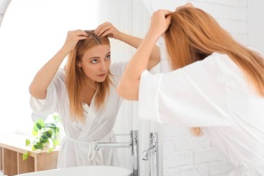 Banyoda aynanın yanında saç dökülmesi sorunu olan olgun bir kadın.