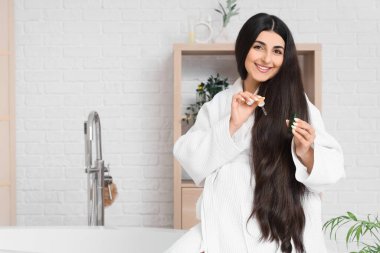 Genç hamile bir kadın banyoda saç uzatmak için serum kullanıyor.