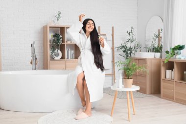 Genç hamile bir kadın banyoda saç uzatmak için serum kullanıyor.