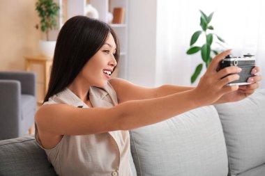 Fotoğraf makineli genç Asyalı kadın evdeki kanepede selfie çekiyor.
