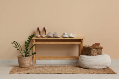 Ayakkabılı bank, çiçekli pouf ve odada bej duvarlı sepet.