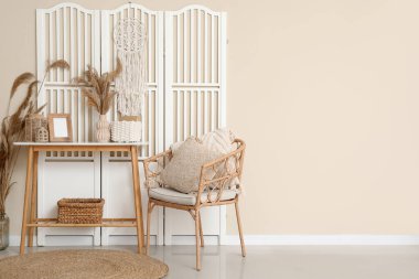 Koltuk, masa ve katlanan ekran bej duvarın yanında.