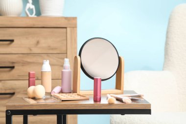 Dekoratif kozmetik ürünleri, makyaj aksesuarları ve oda odasındaki ahşap masanın üzerindeki ayna.