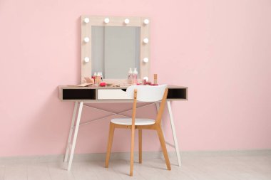 Farklı dekoratif kozmetik ürünleri, makyaj malzemeleri ve pembe duvarın yanındaki sandalyede makyaj masası.